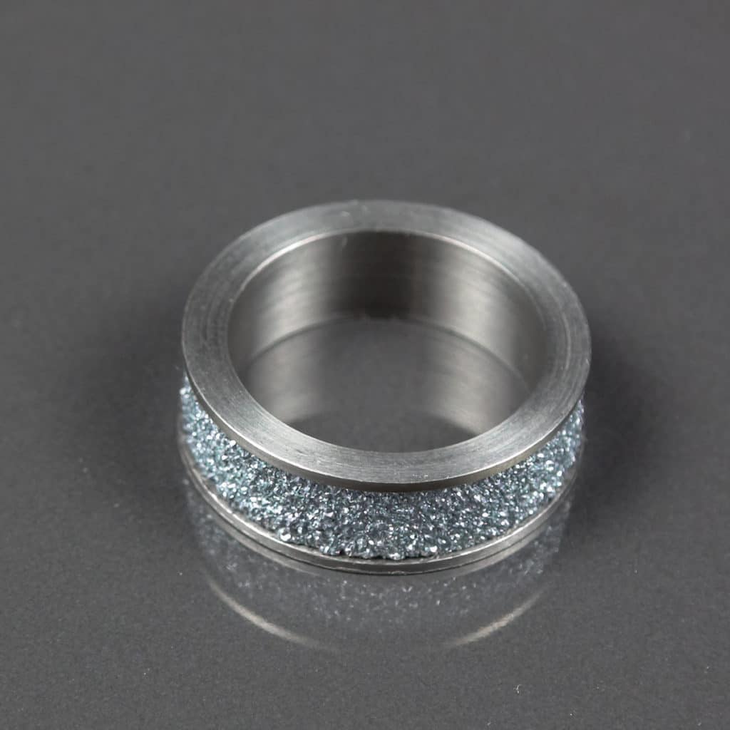 Osmium Produkt und Schmuckstück in Form eines Ringes liegt auf grauer Unterlage