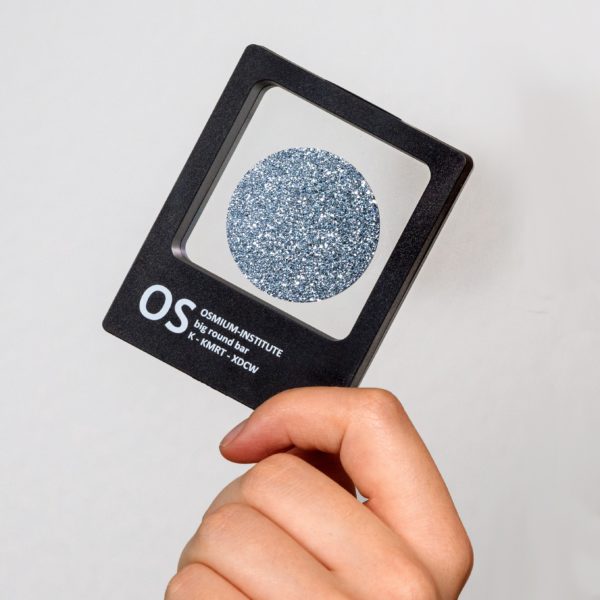 Eine Hand hält diagonal das Produkt Osmium-Disk in der Sichtbox