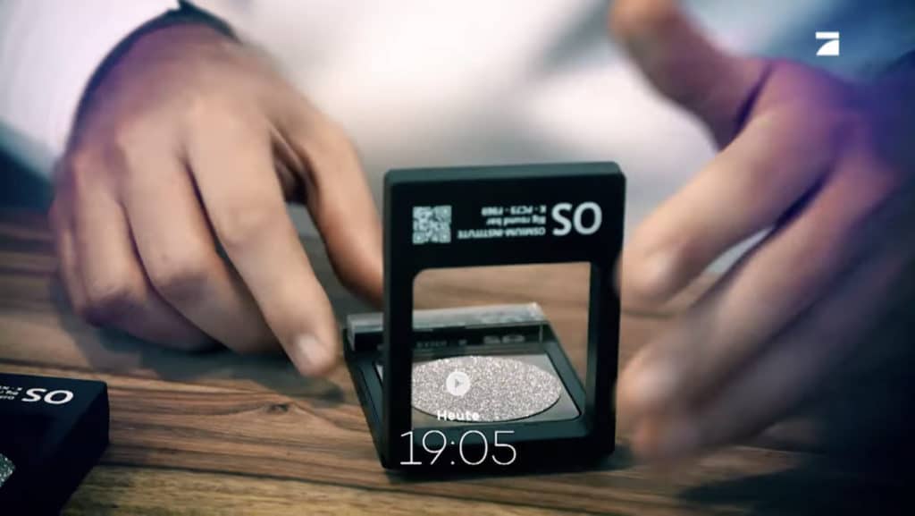 Ein Interessent öffnet eine Osmium-Sichtbox und holt die wertvolle Edelmetall-Disk heraus.